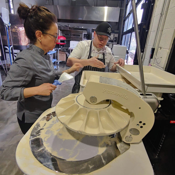 Two people working with a large kitchen appliance in a professional kitchen setting.